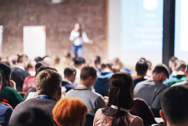 Upcoming Spring Event - View of a Large Group of People Attending a Conference Event with Views of a Female Speaker Presenting in the Front